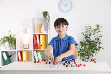 Boy making DNA structure model at desk indoors. Space for text