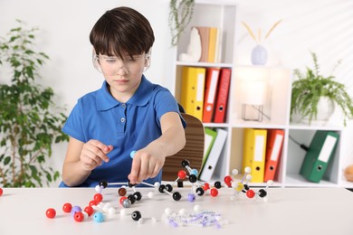 Photo of Boy making DNA structure model at desk indoors. Space for text