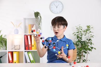 Emotional boy with DNA structure model at desk indoors