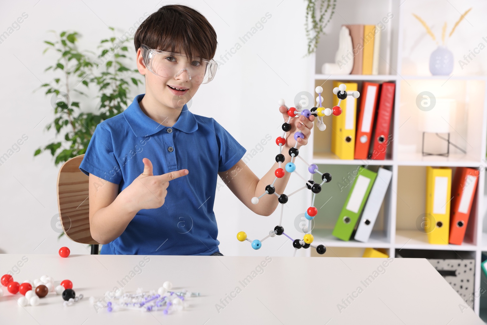 Photo of Boy showing DNA structure model at desk indoors