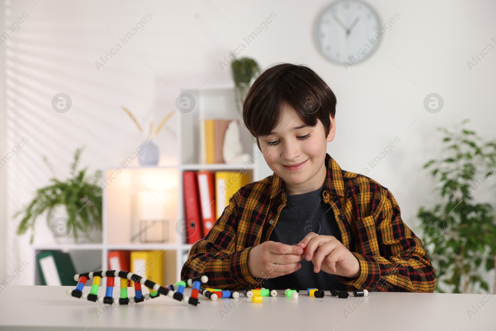 Photo of Boy making DNA structure model at desk indoors. Space for text