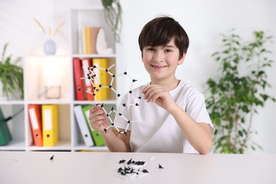 Boy making DNA structure model at desk indoors