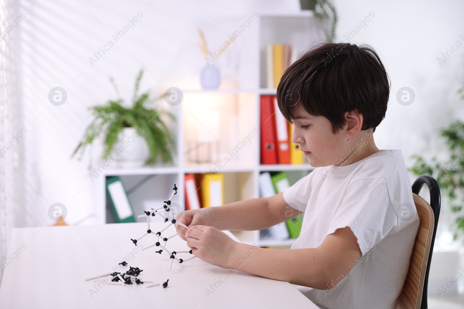 Photo of Boy making DNA structure model at desk indoors. Space for text