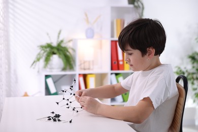 Photo of Boy making DNA structure model at desk indoors. Space for text