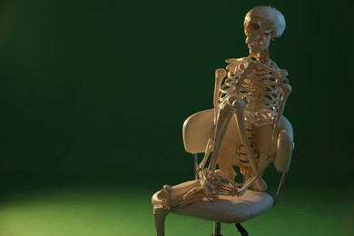 Artificial human skeleton model sitting on chair against green background, space for text