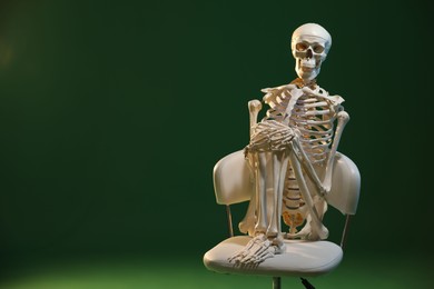 Photo of Artificial human skeleton model sitting on chair against green background, space for text