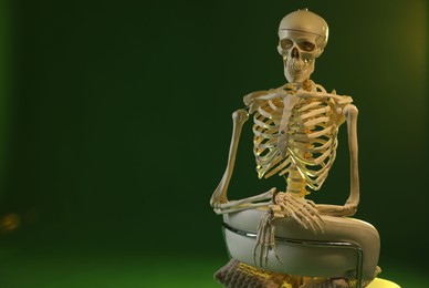 Photo of Artificial human skeleton model sitting and chair on green background, space for text