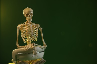 Photo of Artificial human skeleton model sitting and chair on green background, space for text