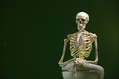 Photo of Artificial human skeleton model sitting and chair on green background, space for text