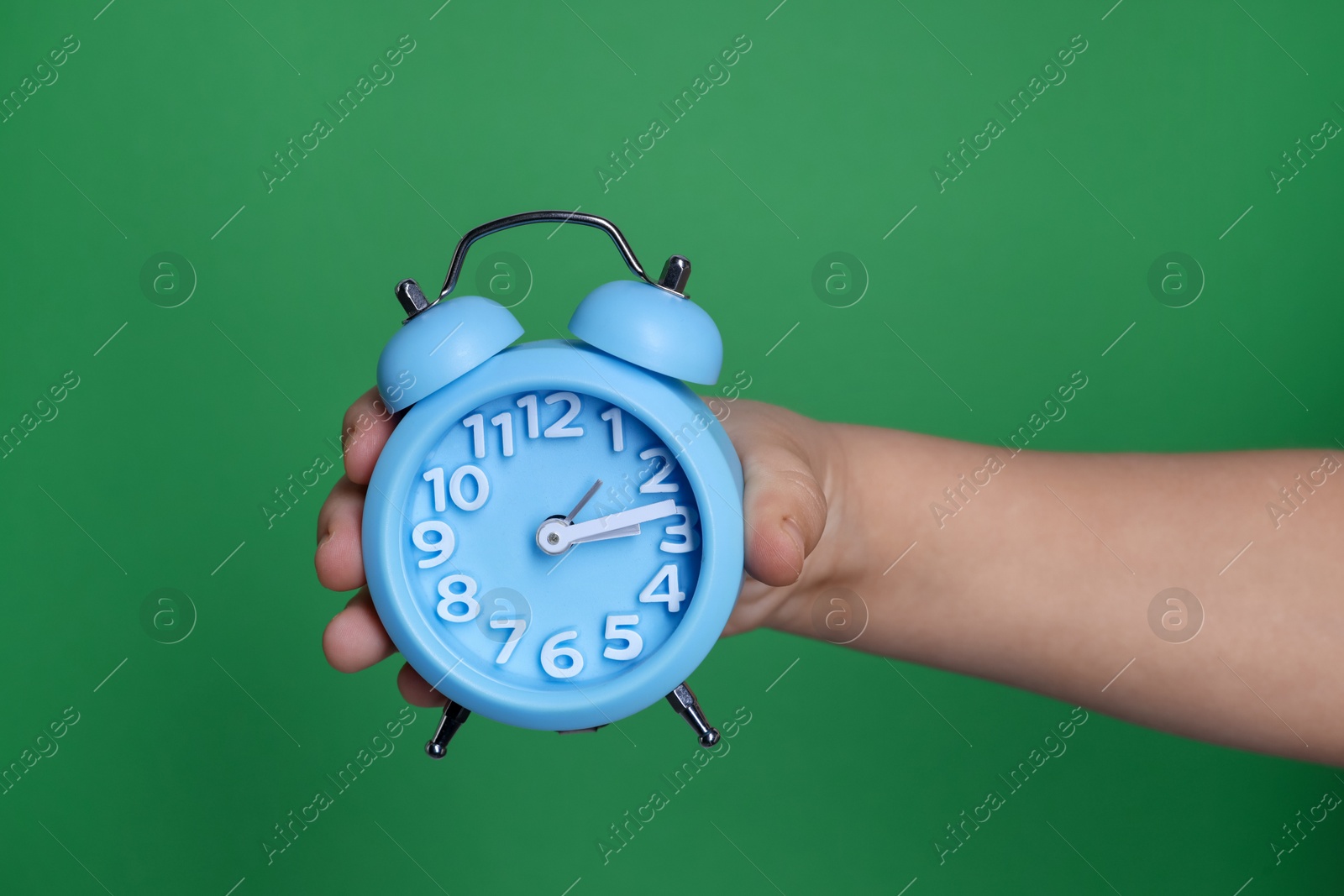 Photo of Child holding light blue alarm clock on green background