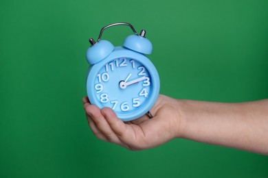 Photo of Child holding light blue alarm clock on green background