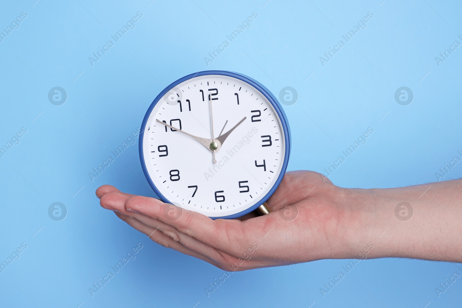 Photo of Man with alarm clock on light blue background, closeup