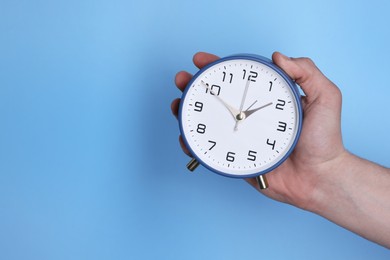 Photo of Man with alarm clock on light blue background, closeup. Space for text