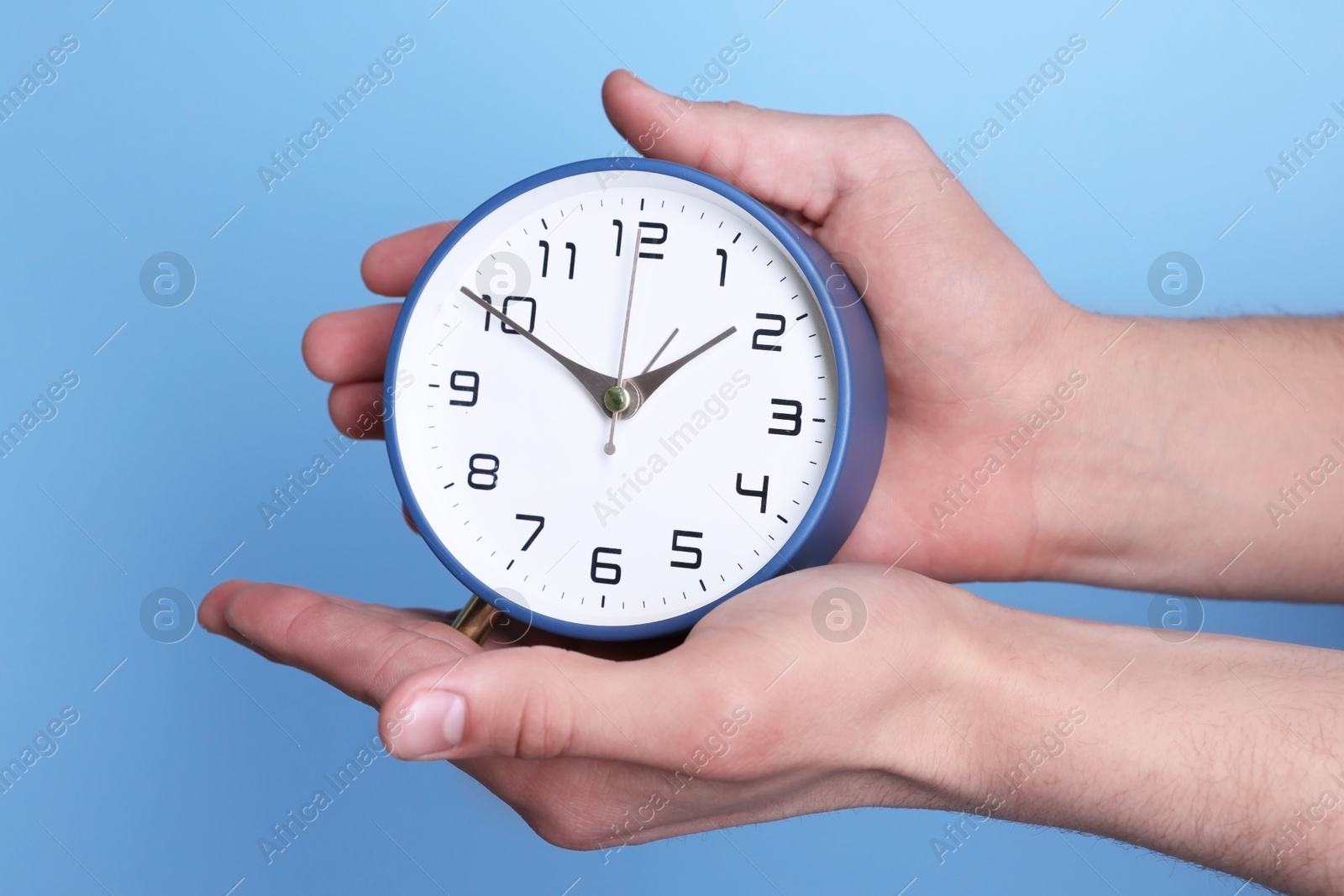 Photo of Man with alarm clock on light blue background, closeup