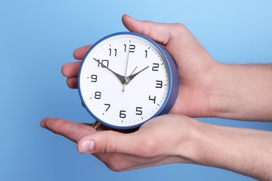 Man with alarm clock on light blue background, closeup