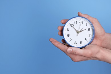 Photo of Man with alarm clock on light blue background, closeup. Space for text