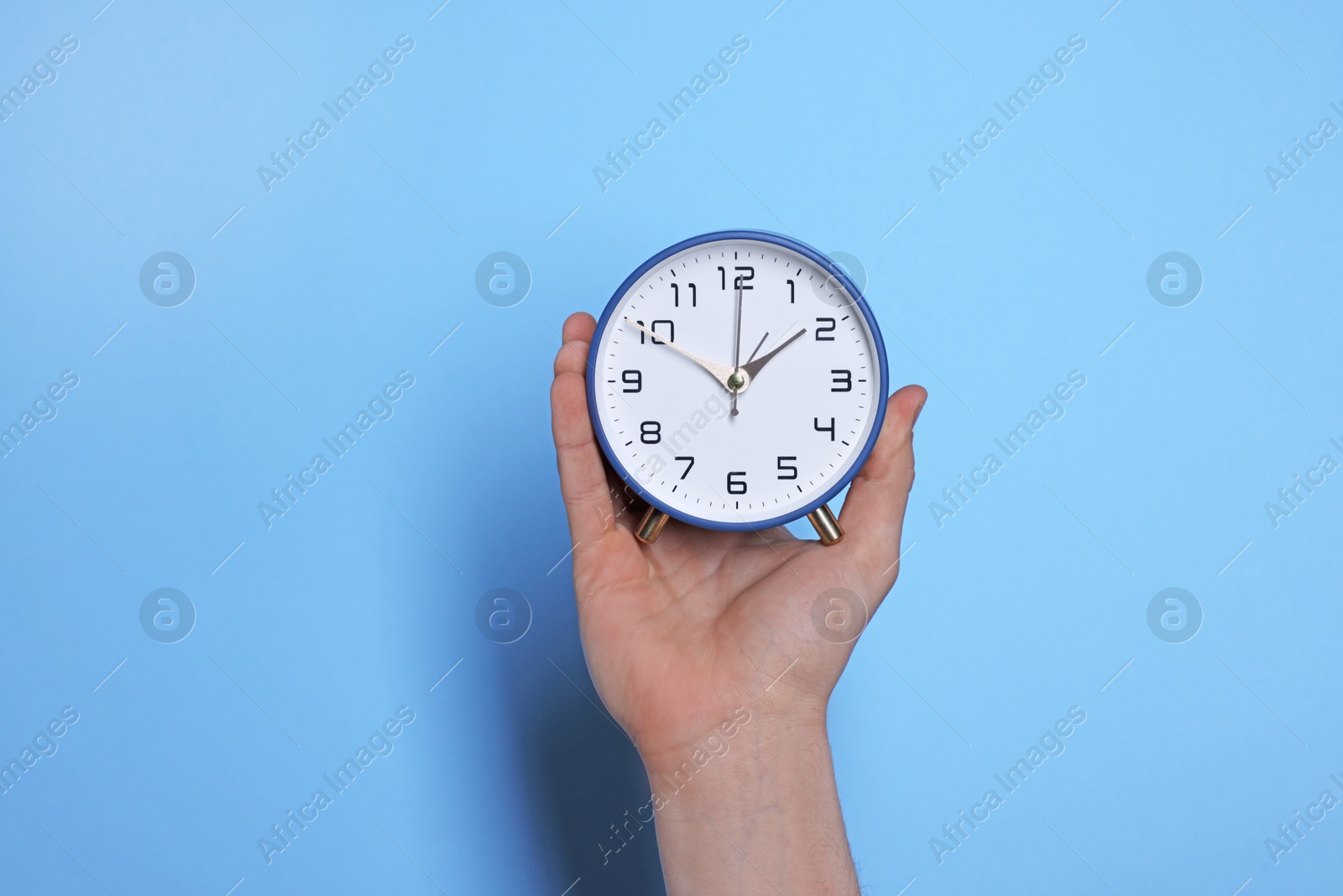 Photo of Man with alarm clock on light blue background, closeup