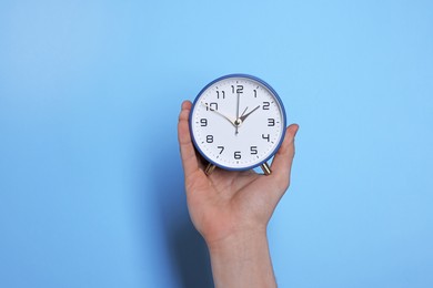 Man with alarm clock on light blue background, closeup