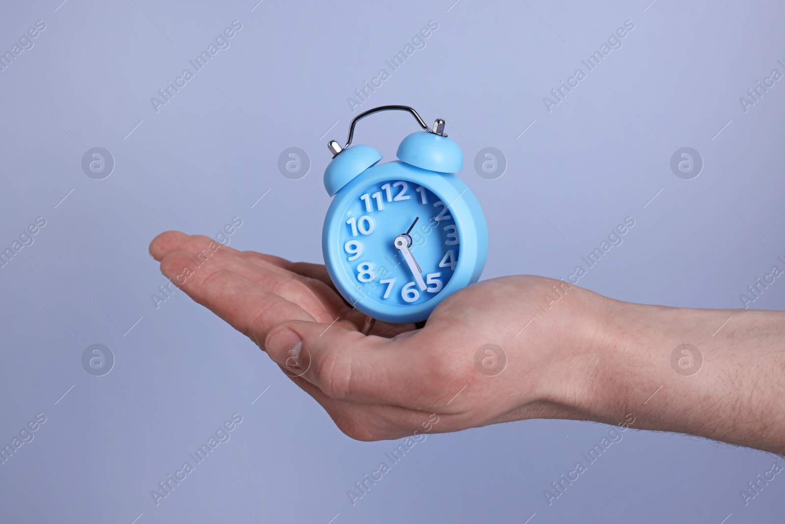 Photo of Man with light blue alarm clock on grey background, closeup