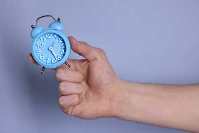 Photo of Man with light blue alarm clock on grey background, closeup