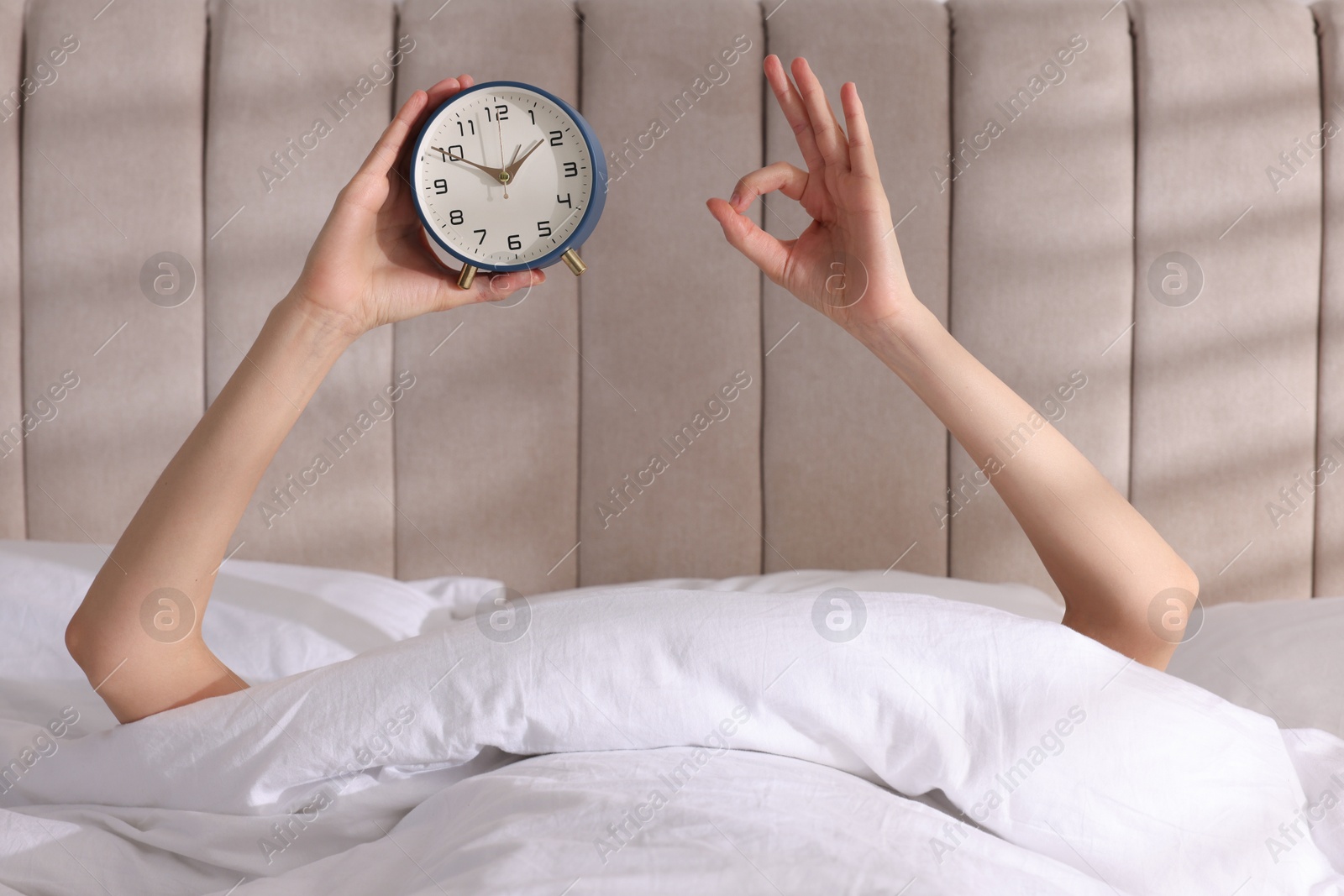 Photo of Woman with alarm clock showing ok gesture in bed at home, closeup. Good morning