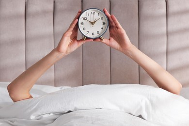 Woman with alarm clock in bed at home, closeup. Good morning