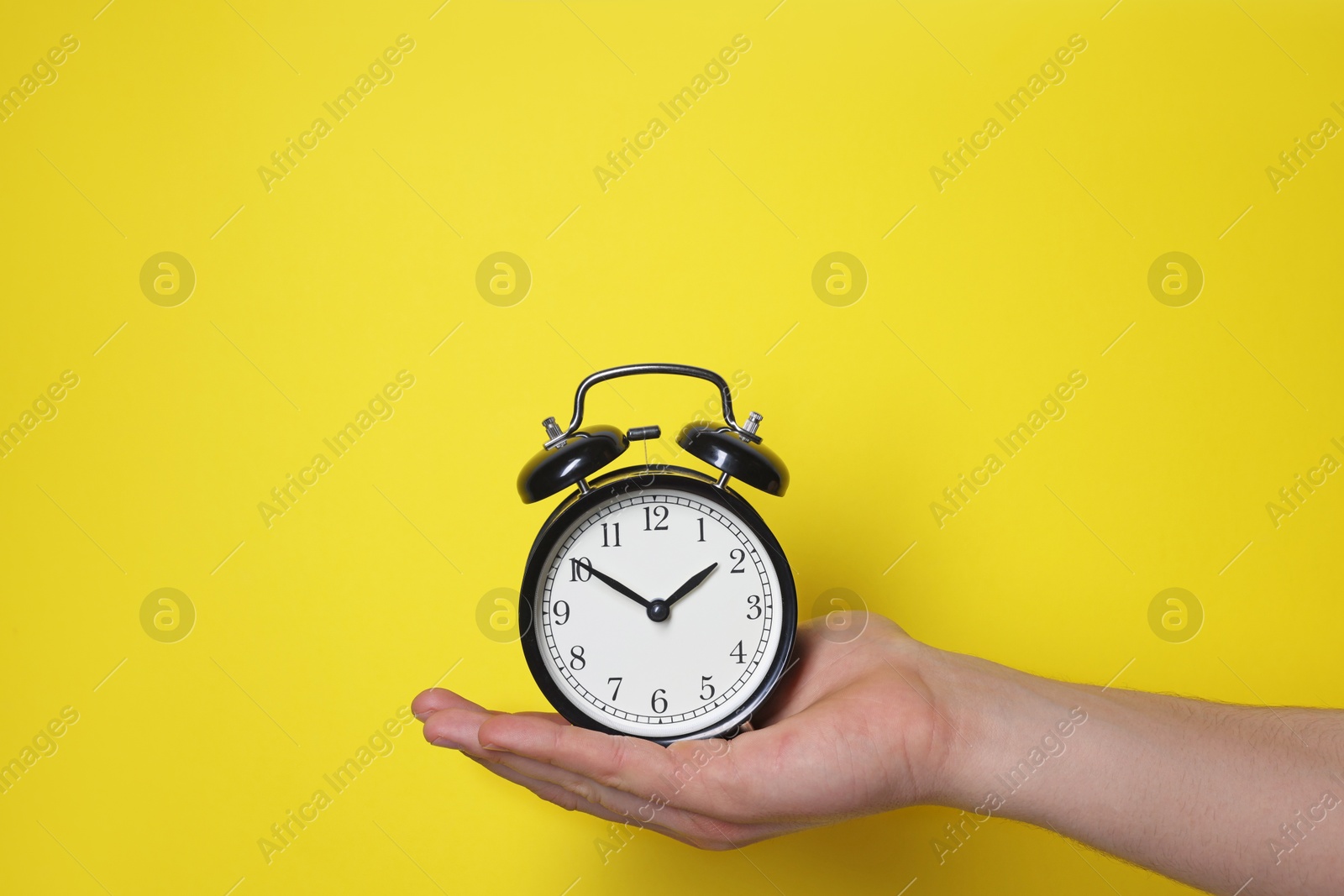 Photo of Man with alarm clock on yellow background, closeup. Space for text