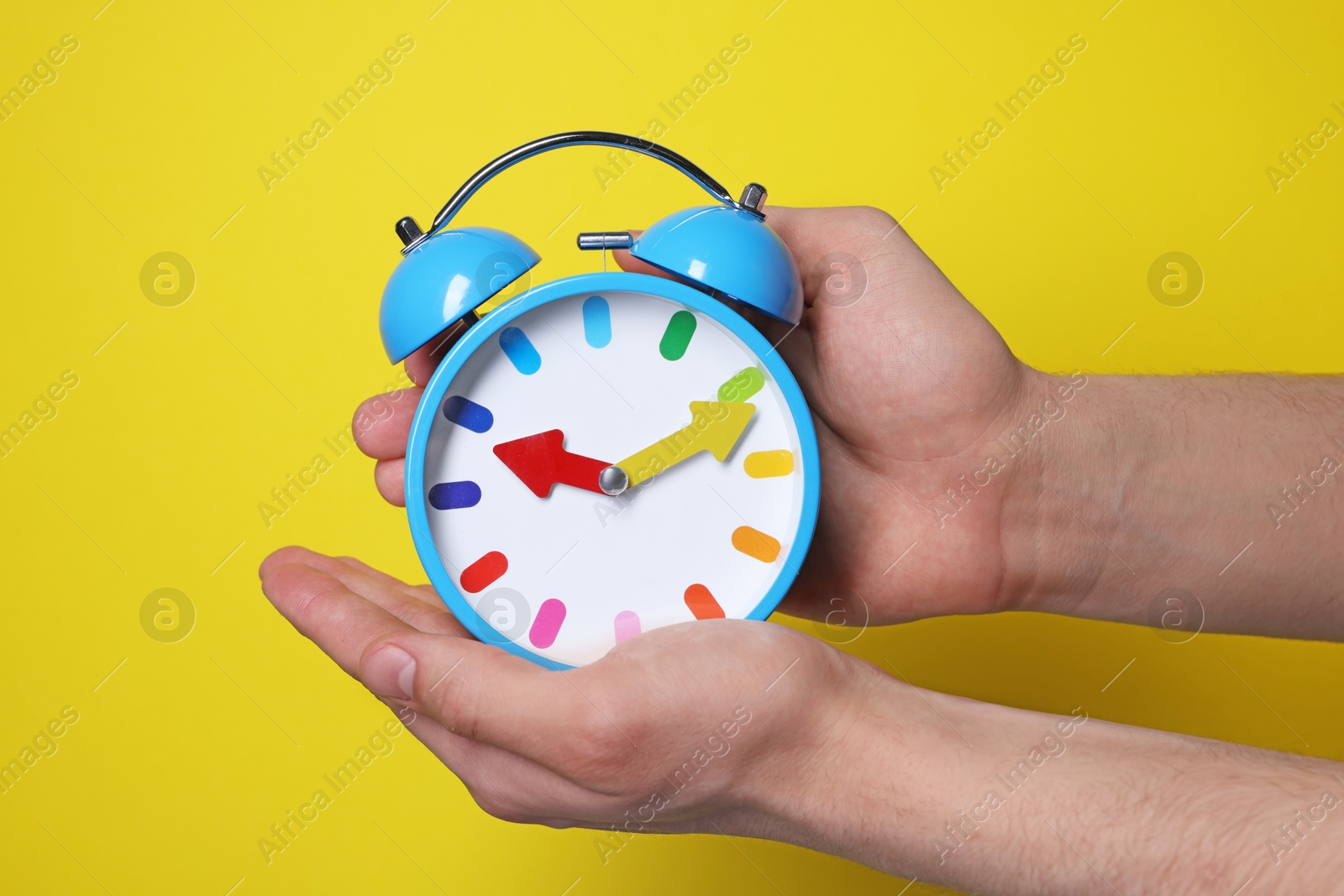 Photo of Man with alarm clock on yellow background, closeup