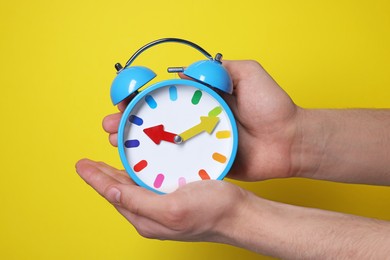 Man with alarm clock on yellow background, closeup