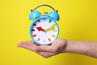 Man with alarm clock on yellow background, closeup