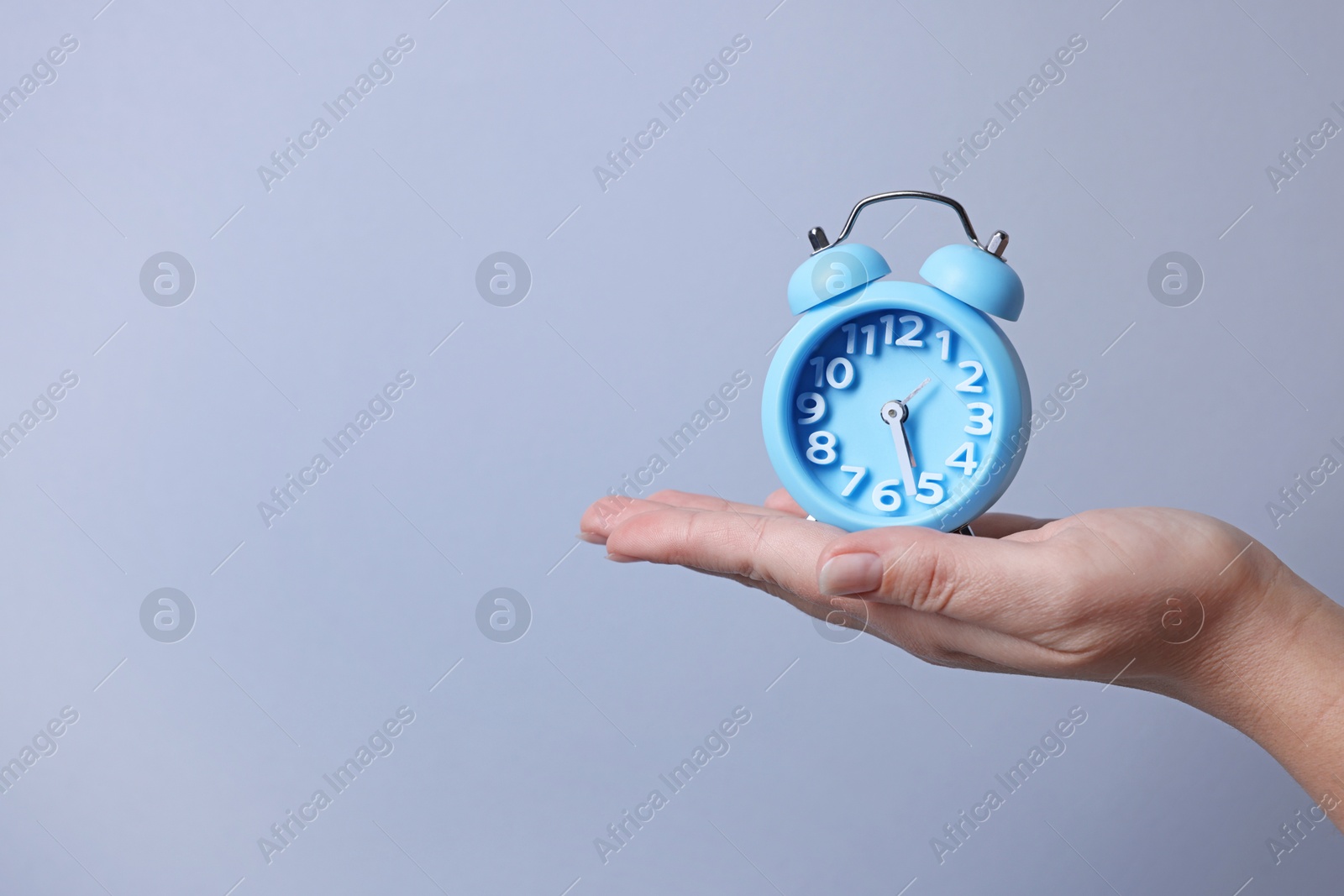 Photo of Woman with alarm clock on grey background, closeup. Space for text