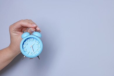 Woman with alarm clock on grey background, closeup. Space for text