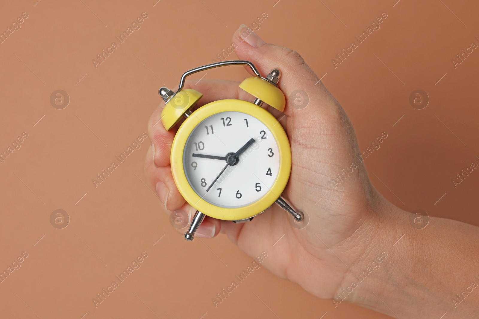 Photo of Woman with alarm clock on brown background, closeup