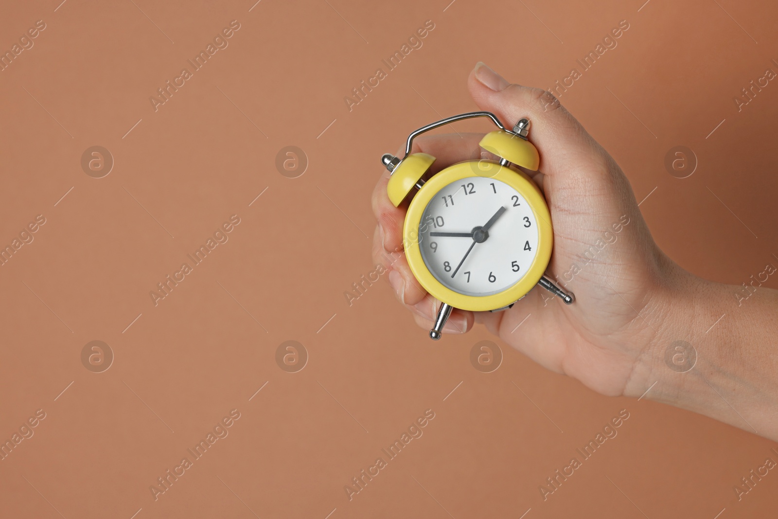 Photo of Woman with alarm clock on brown background, closeup. Space for text