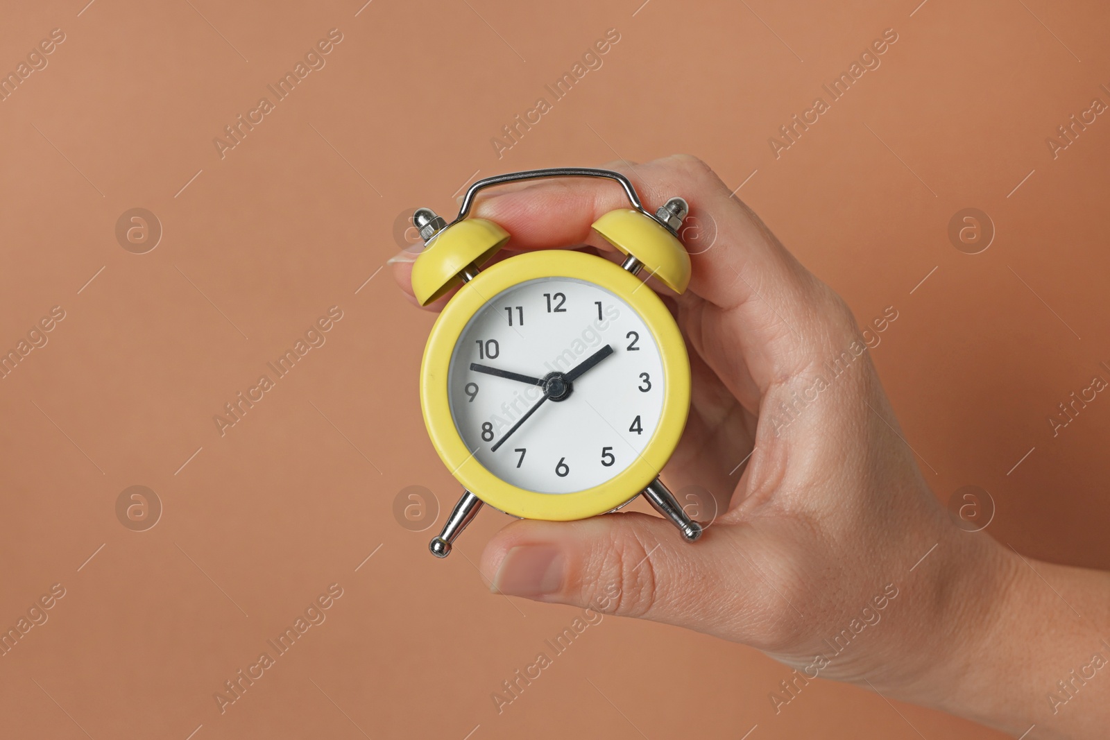 Photo of Woman with alarm clock on brown background, closeup