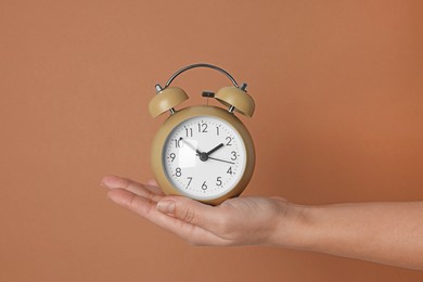 Photo of Woman with alarm clock on brown background, closeup