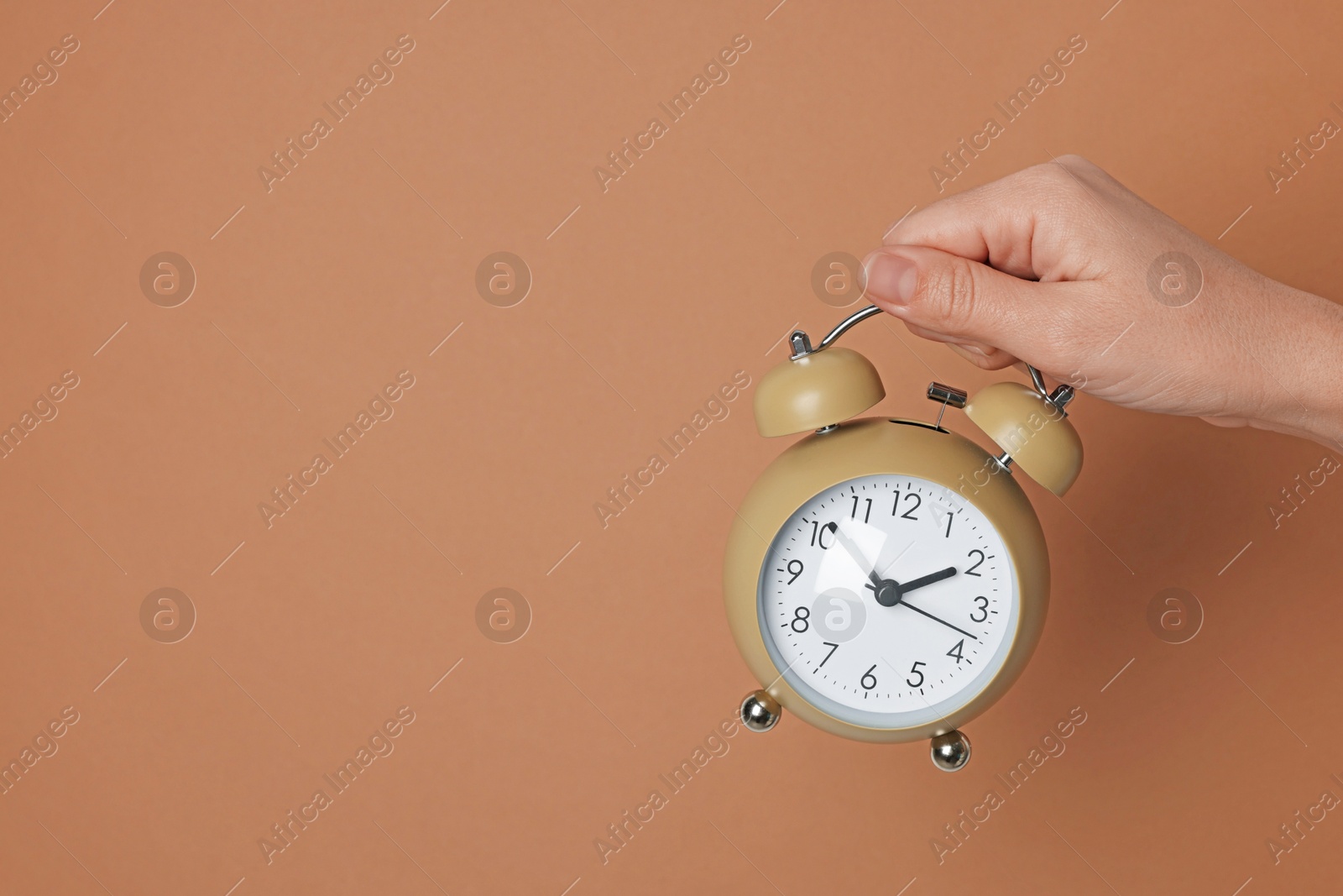 Photo of Woman with alarm clock on brown background, closeup. Space for text