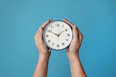 Woman with alarm clock on blue background, closeup