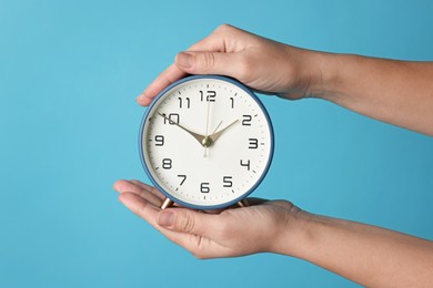 Woman with alarm clock on blue background, closeup