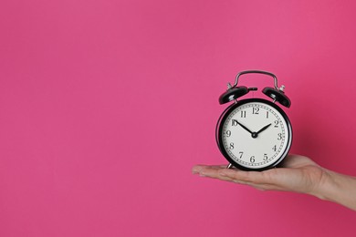 Photo of Woman with alarm clock on crimson background, closeup. Space for text