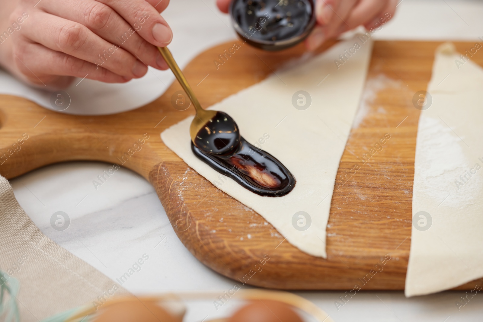 Photo of Woman spreading jam onto fresh dough at white marble table, closeup. Making croissants