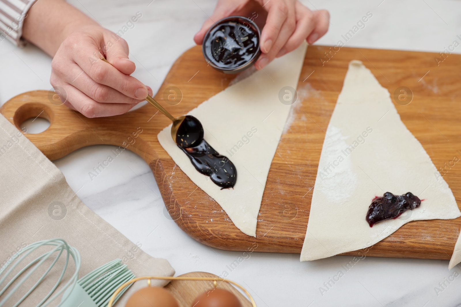 Photo of Woman spreading jam onto fresh dough at white marble table, closeup. Making croissants