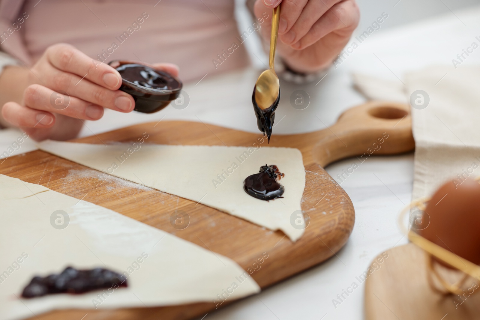 Woman spreading jam onto fresh dough at white table, closeup. Making croissants Photo of Woman spreading jam onto fresh dough at white table, closeup. Making croissants