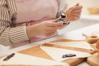 Photo of Woman with jam and fresh dough at white table indoors, closeup. Making croissants