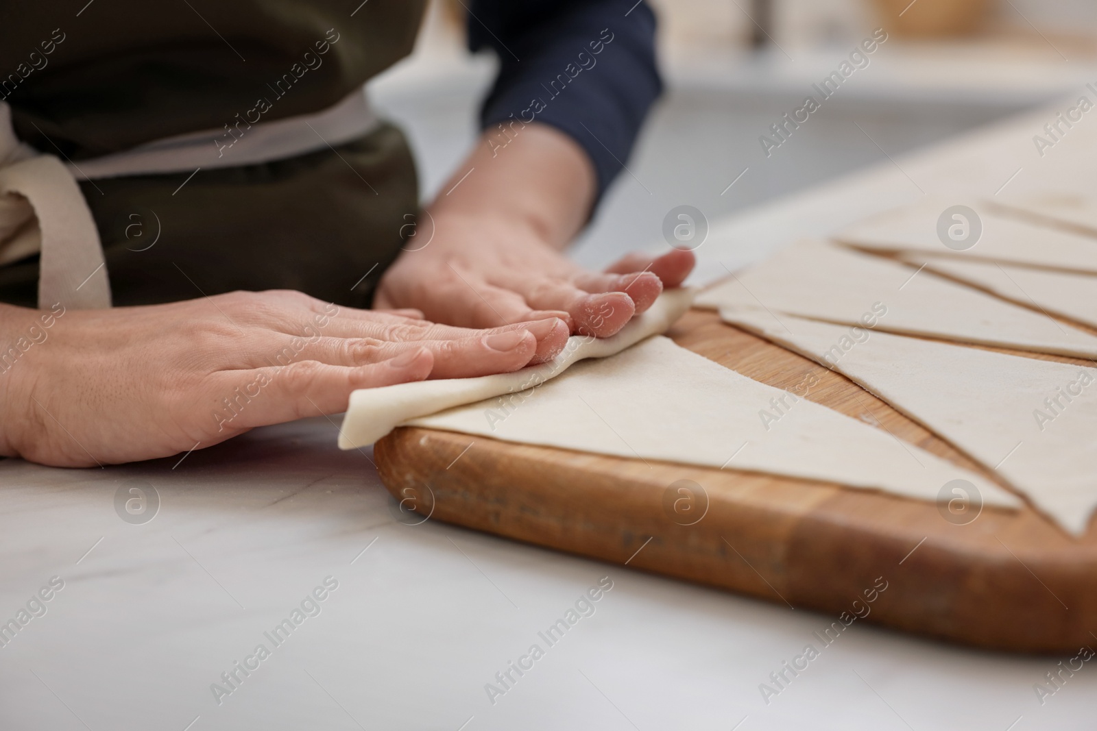 Woman rolling croissant from fresh dough at light table indoors, closeup Photo of Woman rolling croissant from fresh dough at light table indoors, closeup