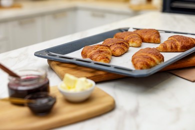 Photo of Freshly baked croissants, butter and jam on white marble table indoors, selective focus