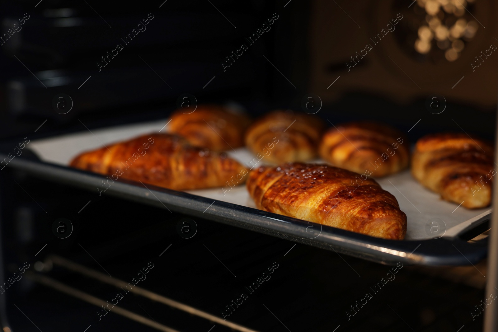 Photo of Freshly baked croissants on baking sheet in oven, closeup