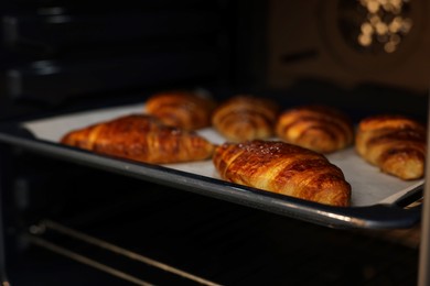 Photo of Freshly baked croissants on baking sheet in oven, closeup