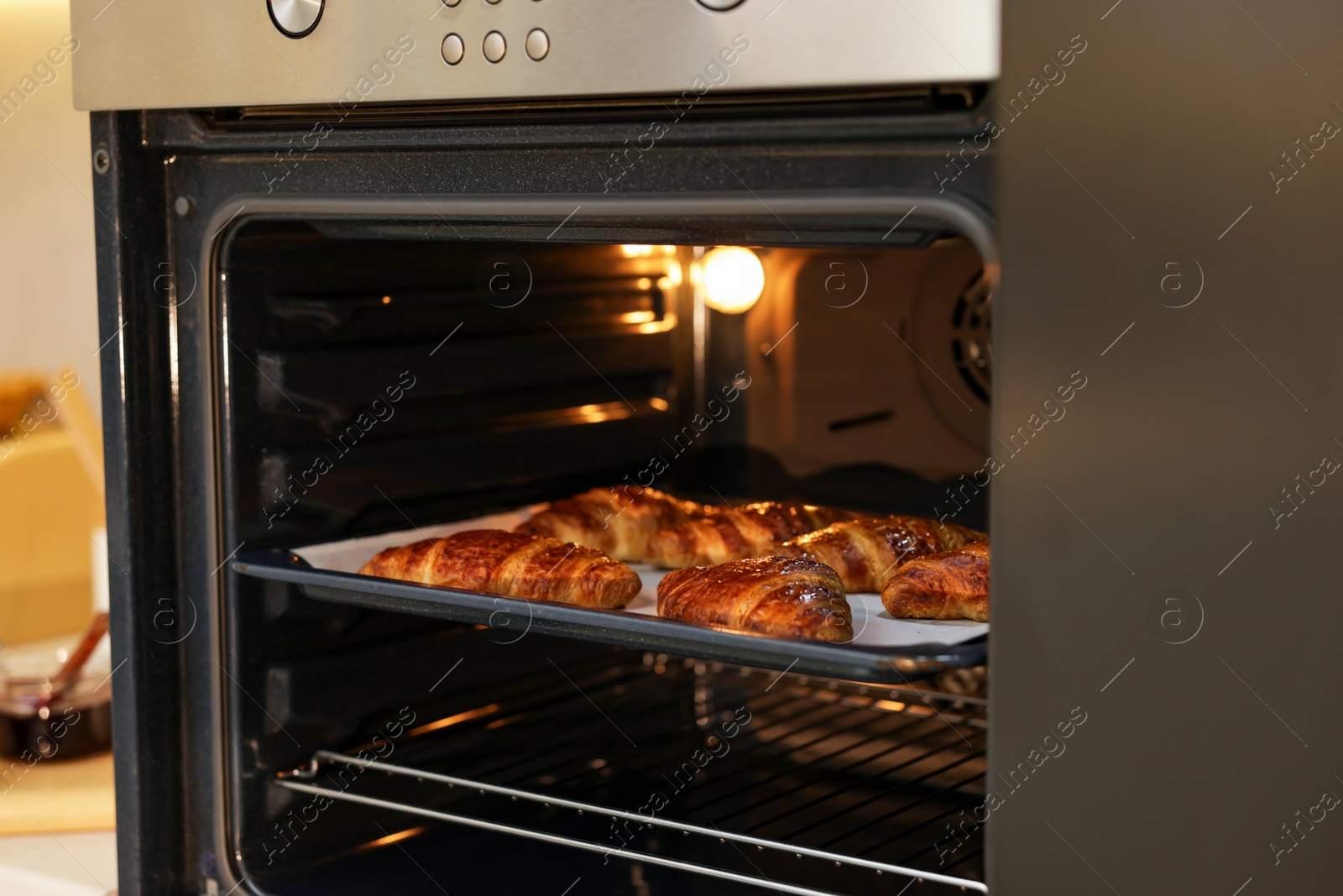 Photo of Freshly baked croissants on baking sheet in oven indoors, closeup