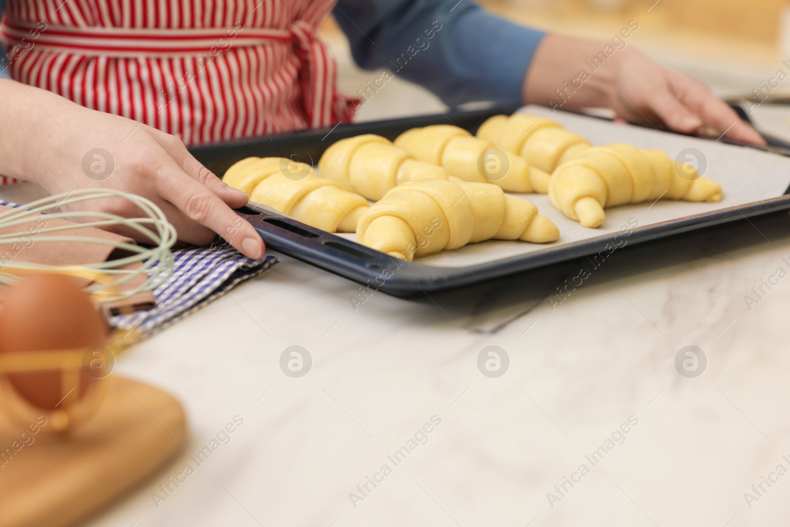 Woman taking baking sheet with raw croissants out of white marble table, closeup Photo of Woman taking baking sheet with raw croissants out of white marble table, closeup